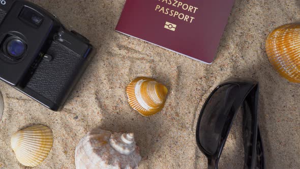 Passport, Vintage Film Camera, Sunglasses and Seashells on Golden Beach Sand.