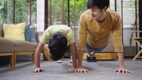 Asian father and son having fun doing exercise push-ups together at home.