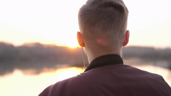 Back View of Man Listens to Music on Beach During Amazing Sunset and Looks to Camera and Smiles