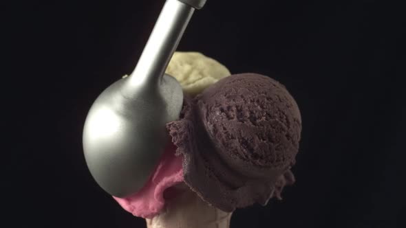 A disher scoop places a strawberry ice cream ball onto a cornette