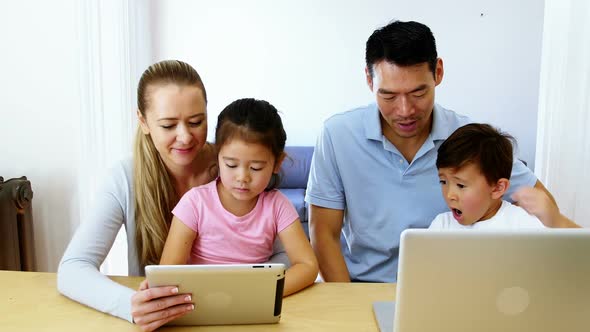 Happy family using digital tablet and laptop in living room alt