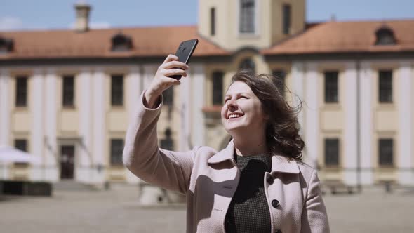 Happy Woman with Freckles Takes Photo on Smartphone of Medieval Castle alt