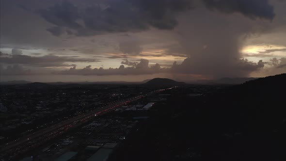 Aerial shot of a highway leading to a hill with a lightning strike on the horizon alt