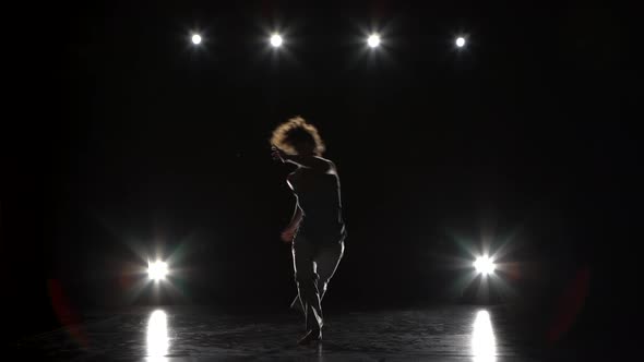 Brunette Female Practicing Capoeira in Darkness Against Spotlight in Studio. alt