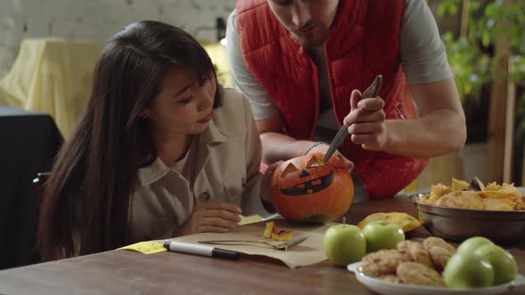 A Young Man Teaches a Lady How to Carve Eyes for a Halloween Pumpkin alt
