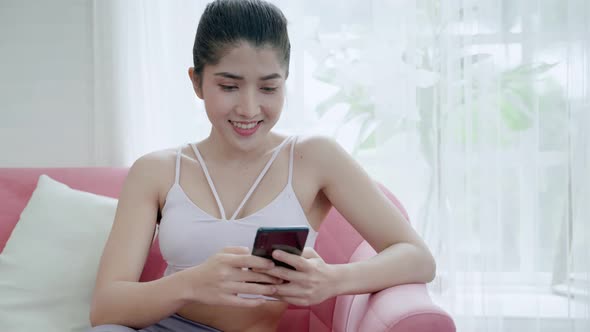 young Asian woman in sportswear uses her smartphone to use social media during a workout break.