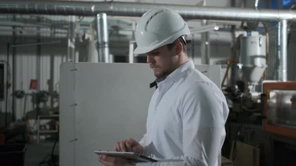 Engineer in Hard Hat is Moving Through a Heavy Industry Factory with a Tablet Computer alt