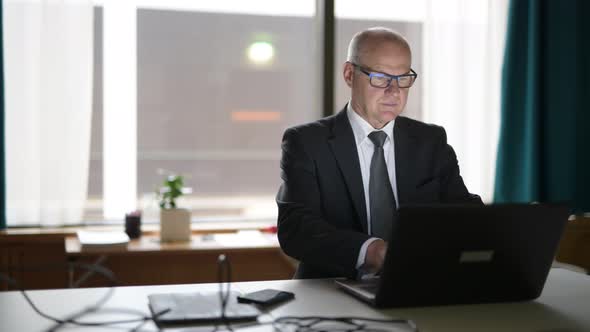 Happy Senior Businessman Using Phone And Laptop At Work alt