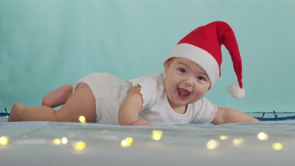 Funny Little Baby Smiling, Cute Infant Boy Wearing Santa Hat Lying on Sofa alt
