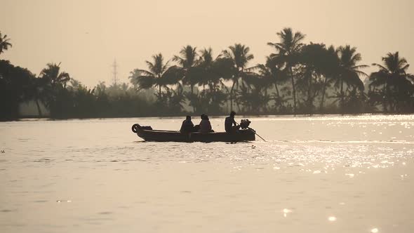 Silhouette of local men on a traditional boat on a river flowing near palm trees, Kerala Backwaters, alt
