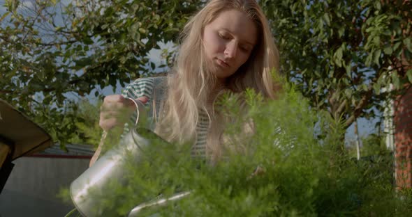 Young Girl with a Watering Can Watering Flowers in a Summer Garden at Sunset