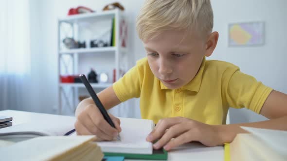 Blond Male Kid Writing Hometask in Notebook and Putting Head on Table, Boredom