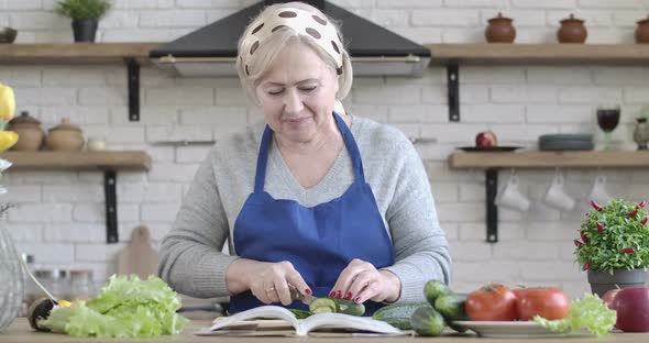 Blond Senior Caucasian Woman Cutting Cucumber and Tasting One Slice, Portrait of Happy Housewife alt