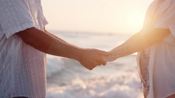 Unrecognizable Couple Holding Hands on Seashore at Sunset Close Up