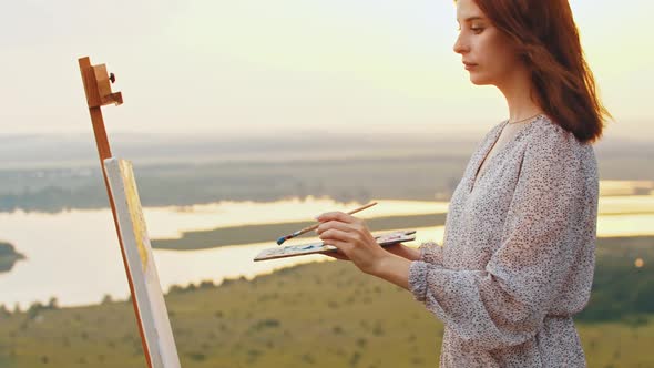 Young Pretty Woman Artist Drawing a Painting on Nature at Sunset Time alt
