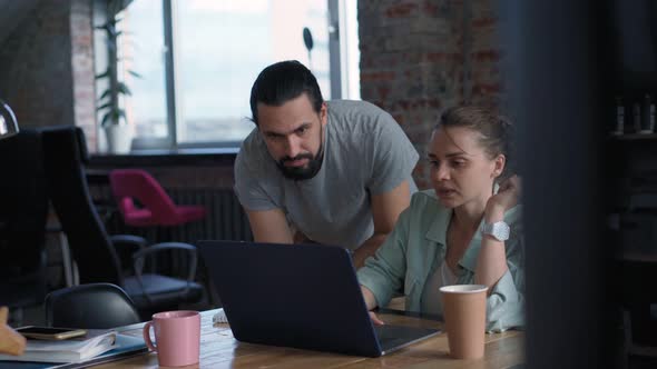 Two Coworkers are Discussing a Project While Sitting in Front of Their Laptops alt
