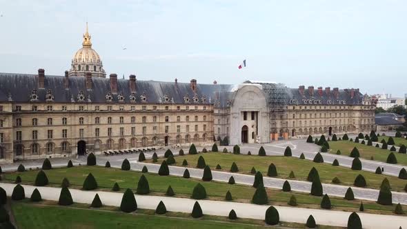 Aerialing: park with lawn, trees and paved paths in front of large complex of historic buildings, Le alt