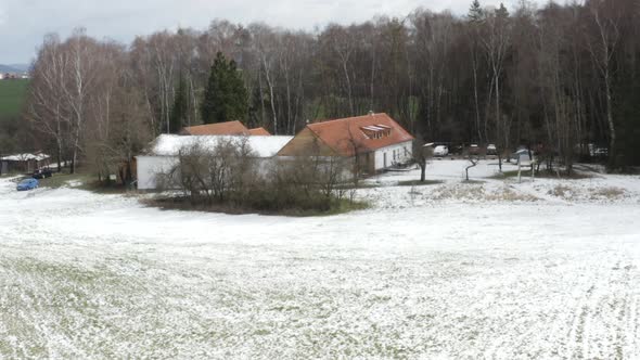 Farmhouse with snowy fields and leafless trees in winter countryside. alt