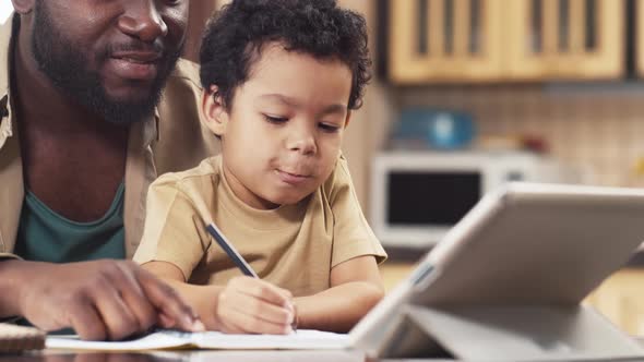 African American man watching his son write in copy-book