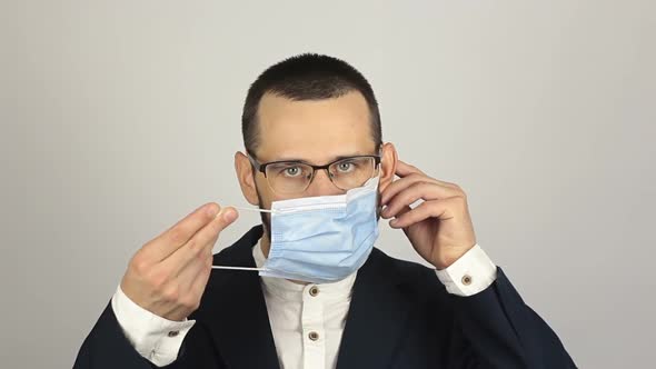 A Young Successful Businessman Puts on a Medical Protective Mask While Talking with Partners.