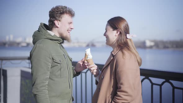 Positive Caucasian Boyfriend and Girlfriend Holding Ice Cream and Chatting Outdoors. Happy Young alt