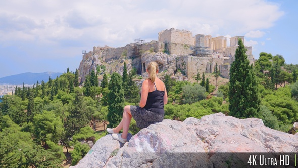 4K Female tourist sitting at Areopagus Hill that looks onto the Acropolis in Athens, Greece alt