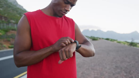 African american man using fitness band while standing on the road alt