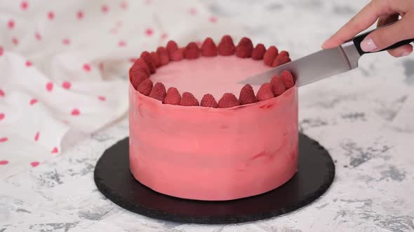 Close-up of woman confectioner cutting a raspberry cake.