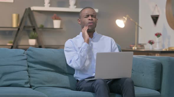 African Man with Laptop Having Toothache on Sofa alt