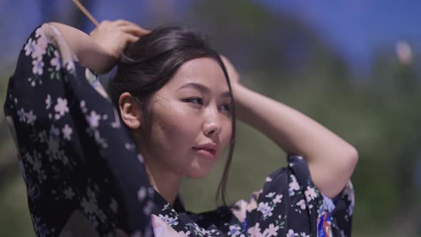 Gorgeous Asian Slim Young Woman Making Buntail Standing in Sunlight in Spring Park Looking Away alt