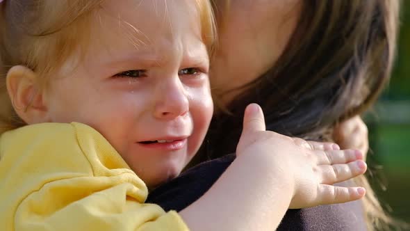 Close-up portrait of a cute crying little girl sitting in her mother arms