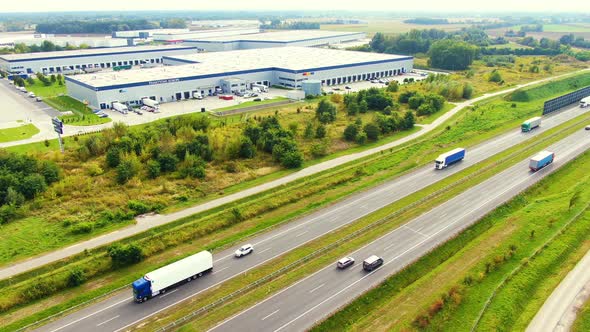 Aerial view of Logistics center next to the highway. Cars drive along the highway. Nearby forests. S alt