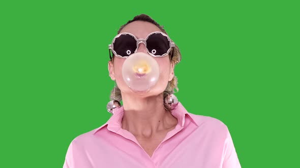 Woman with Party Glasses Chewing Gum Make Bubble On Green Background
