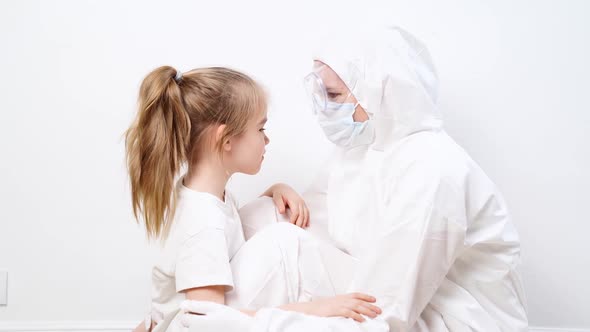 A Little Girl Hugs a Doctor in a White Protective Suit Mask Glasses and Gloves alt