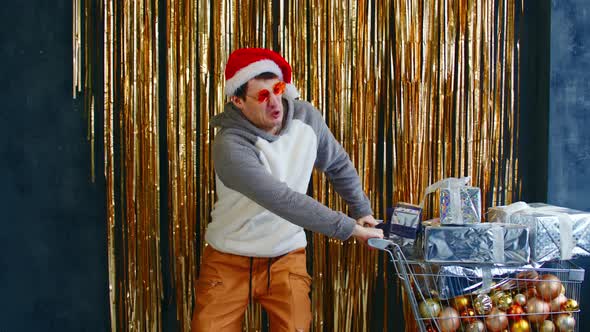Young Male with Shopping Cart Filled of Assorted Baubles and Christmas Presents alt