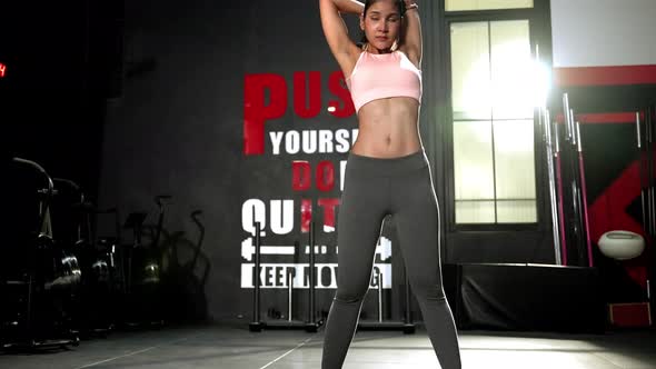 Beautiful Asian woman warming up inside a dark gym. health care concept