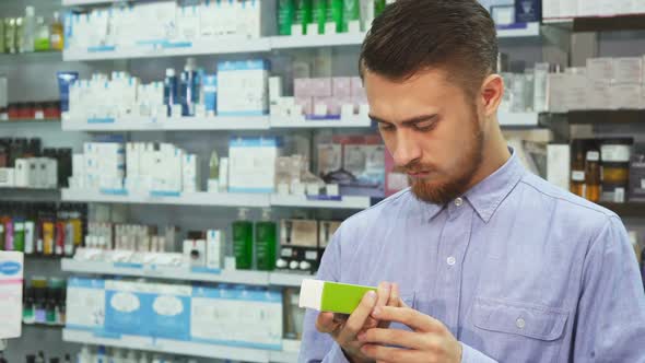 A Young Man Holds a Medicine in His Hand and Reads Something on the Phone  alt