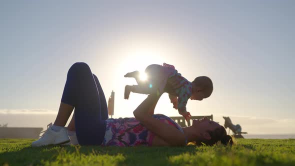 Young Mother Is Keeping on Her Arms and Playing with a Baby Girl on a Ocean Beach at Sunset alt