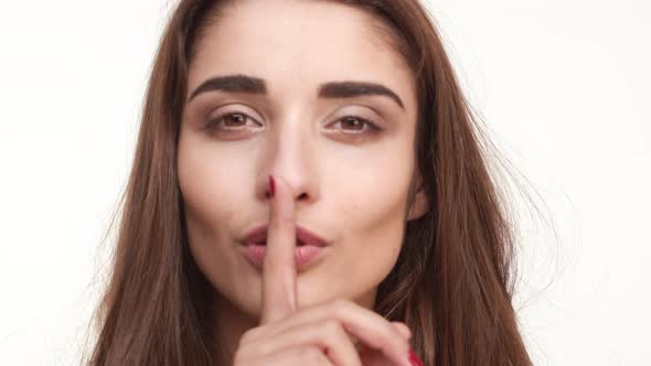 Young Beautiful Caucasian Female with Long Brown Hair Putting Finger to Lips Smiling on White alt