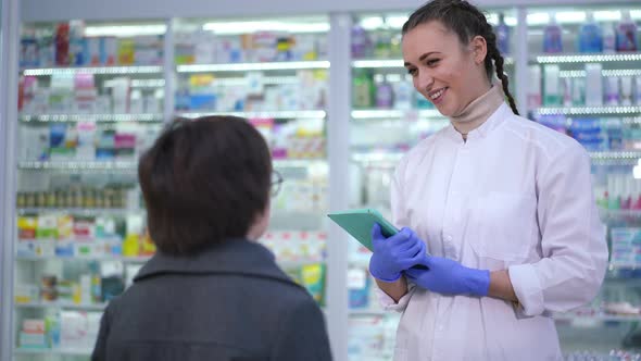 Young Positive Pharmacist Talking with Boy Standing in Drugstore Indoors alt