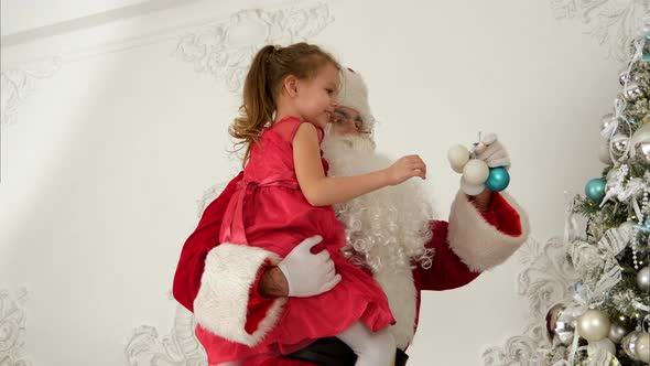 Santa Claus Helping Little Girl To Hang Baubles on Top of the Christmas Tree alt