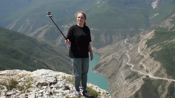 A girl in a black T-shirt shoots herself with an action camera standing on the edg canyon alt