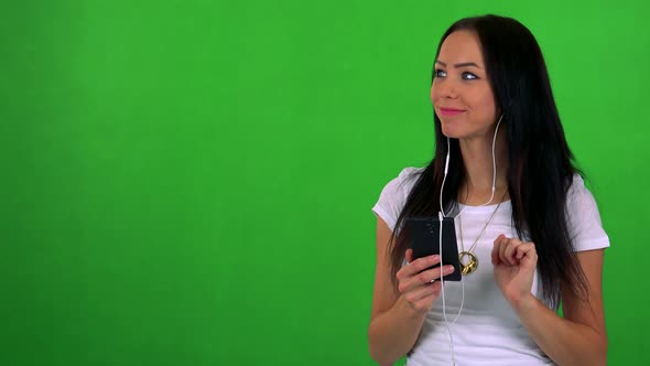 Young Pretty Woman Listens Music with Earphone on Smartphone - Green Screen - Studio alt