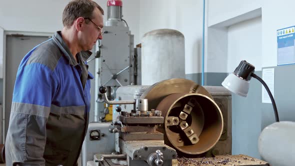 Metal Turner with Glasses Works at Lathe in Production Hall
