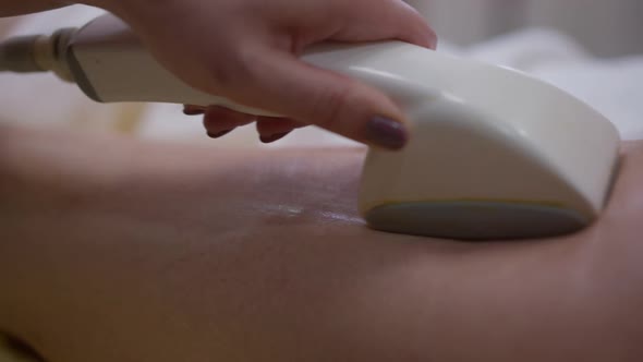 Closeup Anticellulite Massaging Machine in Hand of Professional Masseur Rubbing Skin on Leg of Slim alt