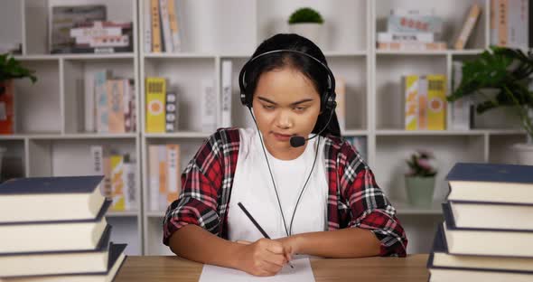 Female student in headphones and glasses talking at camera and note on paper alt