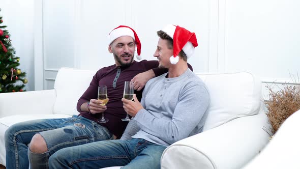 Happy gay male couple celebrating Chritsmas at home sitting on the couch drinking champagne