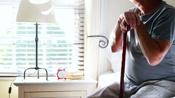Thoughtful senior man with his walking stick in the bedroom alt