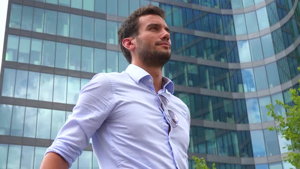 A Businessman Stands in Front of an Office Building and Looks Around Proudly, Closeup From Below alt