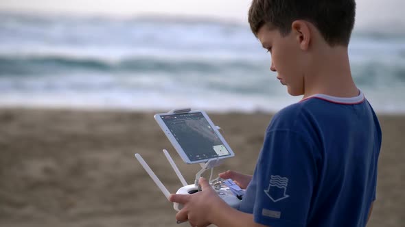 Boy Operating a Drone with Remote Control. Quadrocopter Drone Flying Over Sunset Sea alt